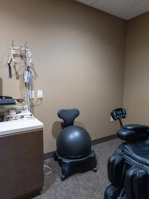 Small medical room with computer, exercise ball chair, and black massage recliner in neutral tones.