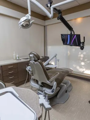 Modern dental office with beige dental chair, overhead light, monitor, and cabinetry under soft lighting.