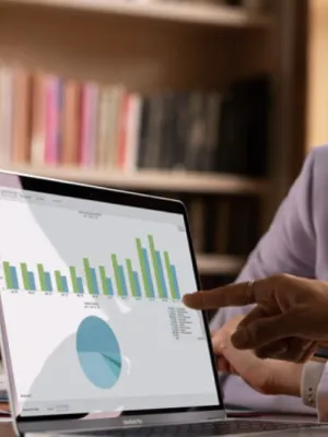 Two professionals analyzing bar and pie charts on a laptop screen in an office setting