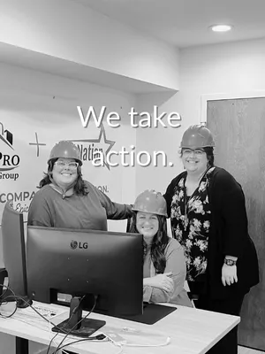 Three women wearing hard hats smiling in an office with computer and motivational wall sign