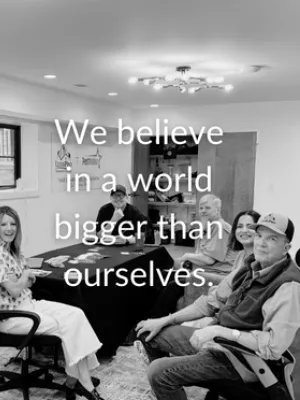 Five people seated around a table in an office with the text We believe in a world bigger than ourselves overlaid.