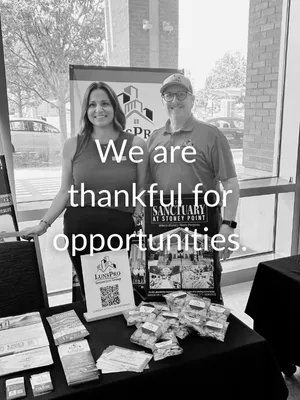 Two smiling people stand behind a table with promotional materials and snacks at Sanctuary at Street Point booth.