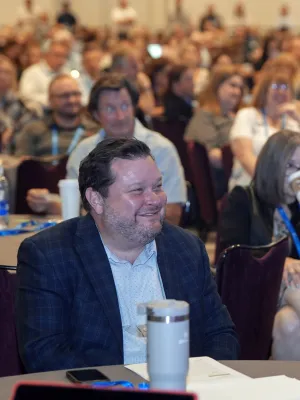 Audience of diverse professionals smiling and listening attentively at a conference or seminar event.