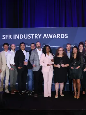 Group of diverse professionals holding awards on stage at SFR Industry Awards event with blue backdrop and curtains.