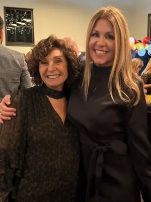 Two women smiling and posing at an indoor event with balloons and gift table in the background