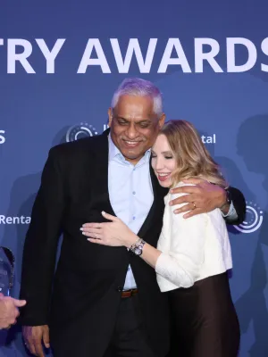 People hugging and smiling at an industry awards event with blue backdrop and white text