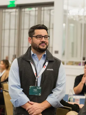 Two men engaged in a professional conversation at a networking event with attendees in the background.