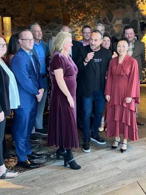 Group of professionally dressed people standing indoors with ambient lighting and stone walls, engaged in conversation.