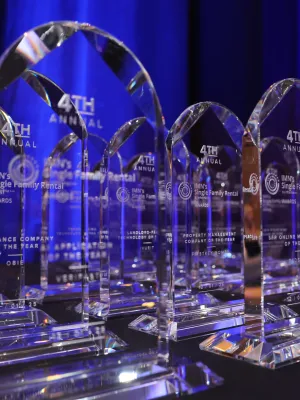 Row of clear glass trophies for the 4th Annual IMN Single Family Rental Awards displayed on a table.