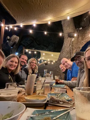 Group of friends enjoying dinner under string lights at an outdoor restaurant with warm, festive ambiance.