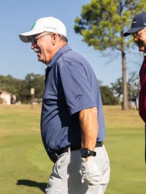 Three elderly men enjoying a sunny day playing golf on a green course with clear blue sky