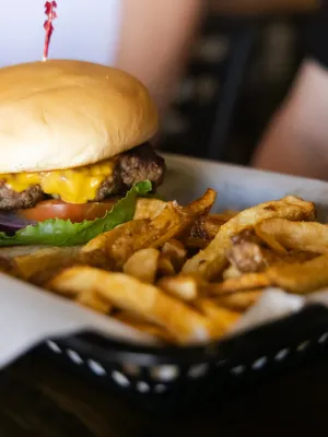 Cheeseburger with lettuce and tomato served with curly fries in a basket on a table.