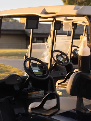 Golf carts parked near a clubhouse on a green course at sunset with warm natural lighting.
