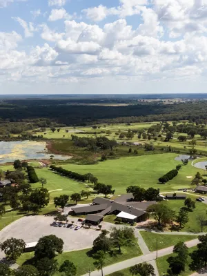 Aerial view of a golf course with green fairways, water hazards, trees, and clubhouse under a cloudy sky.