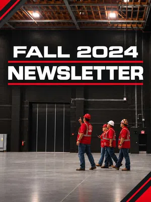 Four construction workers in red safety gear walk inside a large industrial building under Fall 2024 Newsletter text.
