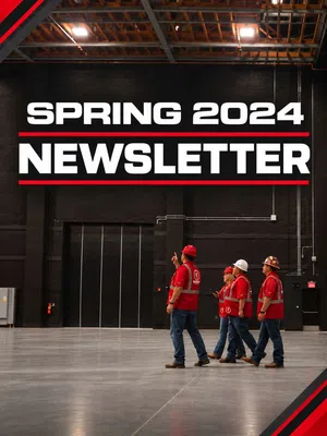 Group of workers in red safety gear walking inside a large industrial warehouse with Spring 2024 newsletter text above.