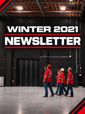 Four construction workers in red vests and helmets walk inside a large industrial building under Winter 2021 Newsletter text.