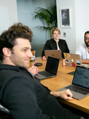 Diverse group of professionals collaborating around a conference table with laptops in a modern office.