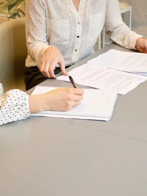 Two women in polka dot shirts working on documents and notes at a gray office table.