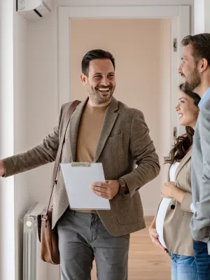 Real estate agent showing a smiling couple a bright modern apartment with large glass doors and wooden floors.