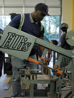 Worker operating Ellis metal cutting machine in a busy industrial workshop with colleagues in the background