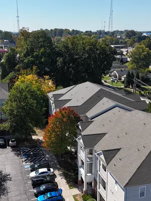 Aerial view of suburban apartment buildings with parking lots, trees, and a clear blue sky on a sunny day.