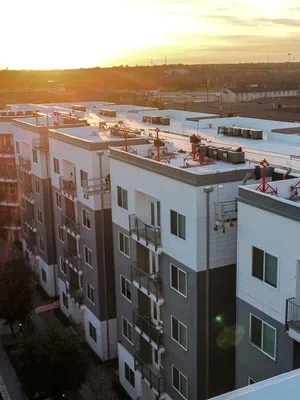 Modern apartment complex with rooftop HVAC systems at sunset and urban landscape in the backgroundAerial view of Mattco white single-ply flat roof on a mid-rise multi-family apartment complex at sunset