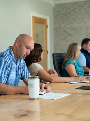 Four professionals seated at a conference table engaged in a business meeting with notes and laptops.