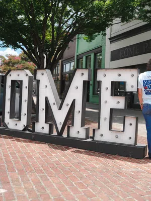 Person leaning on large illuminated letters spelling ROME on a brick sidewalk outside Rome PAM Studios.