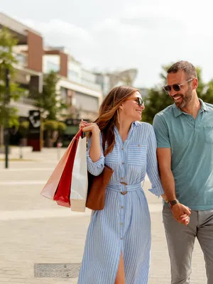 Happy couple holding hands and carrying shopping bags while walking outdoors on a sunny day.