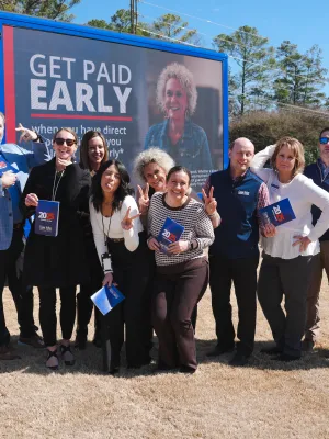 Group of smiling people posing in front of a Coosa Valley Credit Union van with Get Paid Early signage.