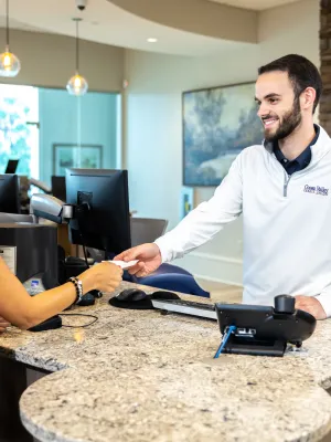Customer handing a card to a smiling male bank teller at a modern bank counter with computers and decor.