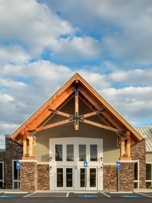 Front entrance of modern building with wooden beams, stone accents, glass doors, and handicapped parking spaces.