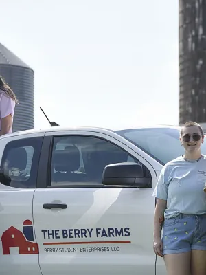 Group of young people standing around a Berry Farms truck with farm silos in the background on a sunny day