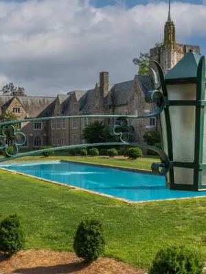 Historic stone building with clock tower, central blue reflecting pool, green lawn, and ornate black lantern in foreground.