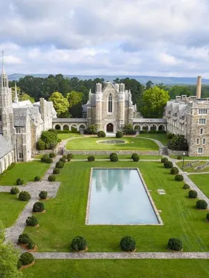 Aerial view of a historic university campus with stone buildings, green lawns, and a rectangular reflecting pool.