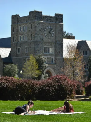 Two women lying on a blanket studying on green lawn with historic clock tower building in background on sunny day