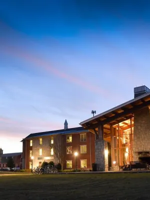 Modern campus buildings with large glass windows lit at dusk under a clear blue sky with fading sunset hues.