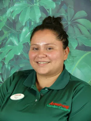 Smiling Armstrong Garden Centers employee wearing green uniform with leafy plant background