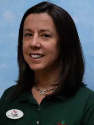 Smiling woman with dark hair wearing a green shirt and silver heart necklace against a blue background
