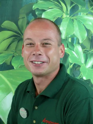 Smiling man in green polo shirt with Armstrong logo posed against large green leafy plant background.