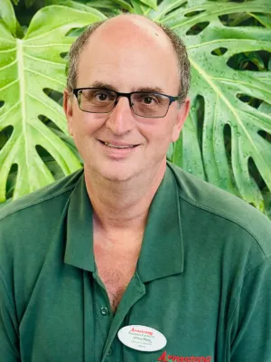 Middle-aged man with glasses wearing a green polo shirt standing in front of large tropical green leaves.