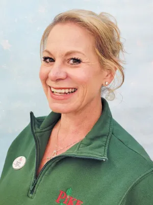 Smiling woman in green Pike Nursery fleece jacket with name badge against a light blue background