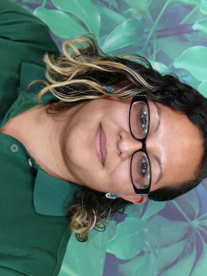 Woman wearing green Armstrong Garden Centers polo and name tag stands against leafy green backdrop