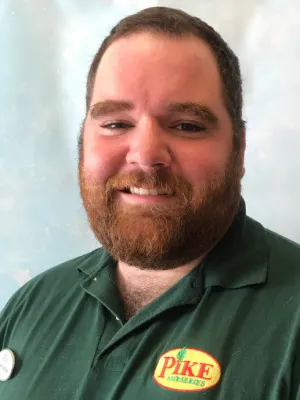 Smiling man with beard wearing a green Pike Nurseries polo shirt and name badge against a light background
