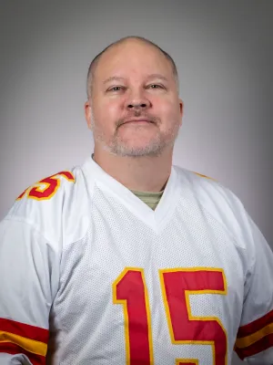 Smiling man in red Georgia Bulldogs jersey and hat standing next to cardboard cutout of enthusiastic football coach.