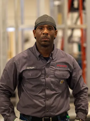 Confident male worker in gray uniform and cap standing in industrial workspace with metal structures.