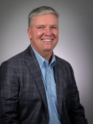 Smiling middle-aged man in a plaid blazer and blue shirt against gray background portrait