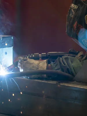 Welder wearing helmet and gloves welding metal with bright sparks and smoke in a workshop environment