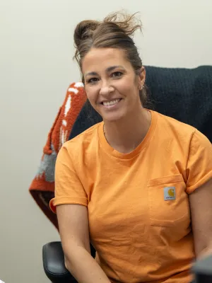Smiling woman in an orange Carhartt t-shirt sitting on a chair with a black and orange blanket behind her